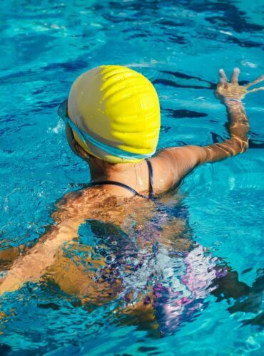 A swimmer wearing a yellow cap enjoying a pool swim captured from the back, highlighting effective technique.